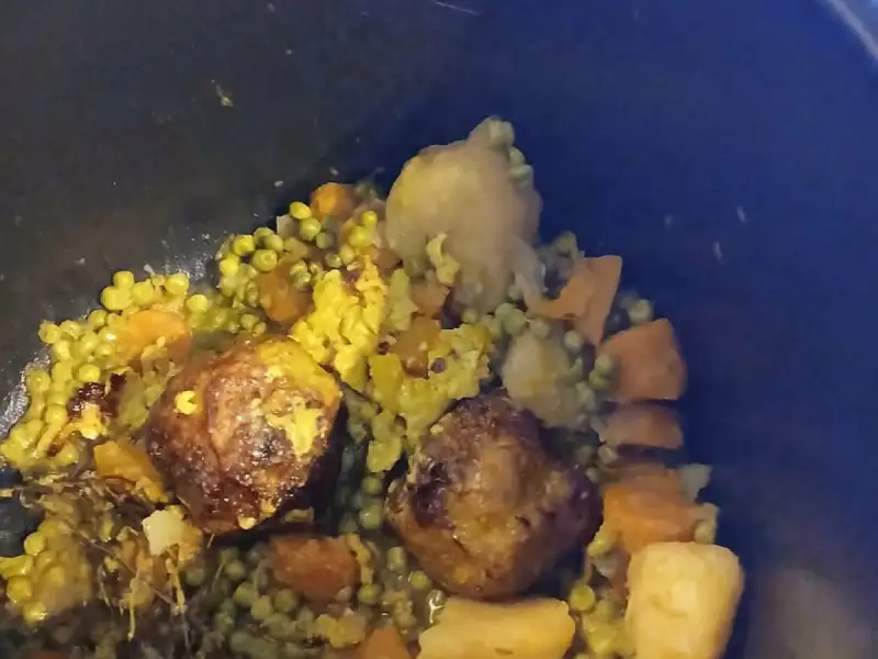 Albóndigas con chícharos, zanahorias y papas con cúrcuma cocinadas a fuego lento en una olla de hierro negra