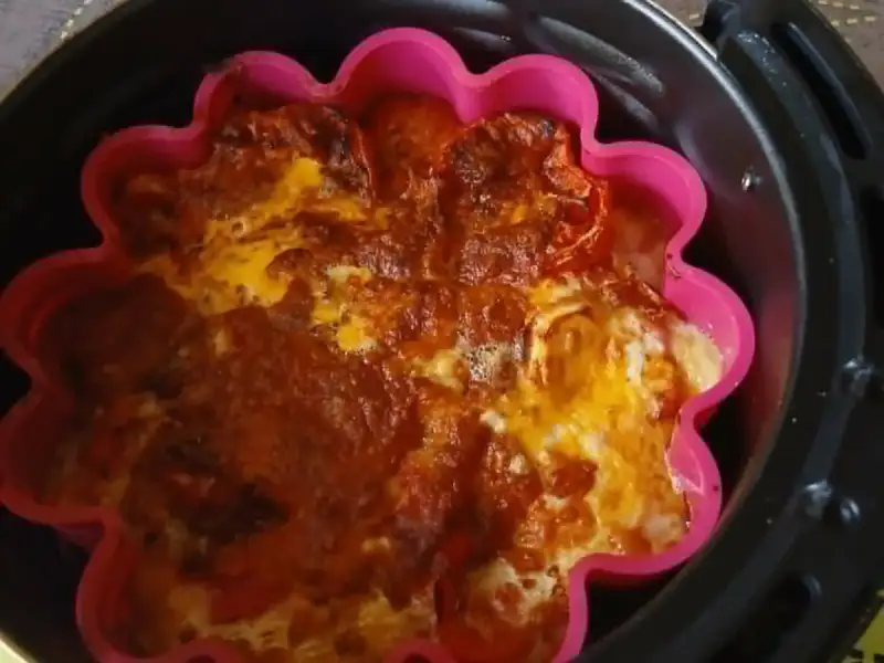 Clafoutis de tomate con queso gratinado en un molde de silicona rosa, en la canasta de una freidora de aire