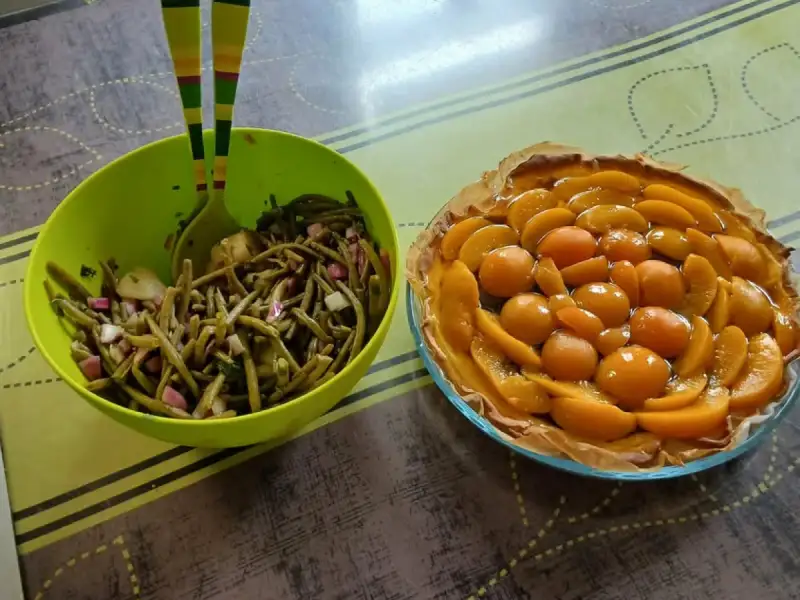 Ensalada de ejotes con cebolla morada y pepino en una ensaladera verde, junto a una tarta de duraznos