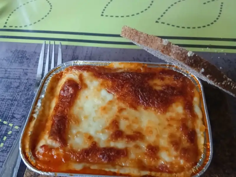Lasañas individuales caseras: una charola de aluminio bien gratinada con una rebanada de pan tostado