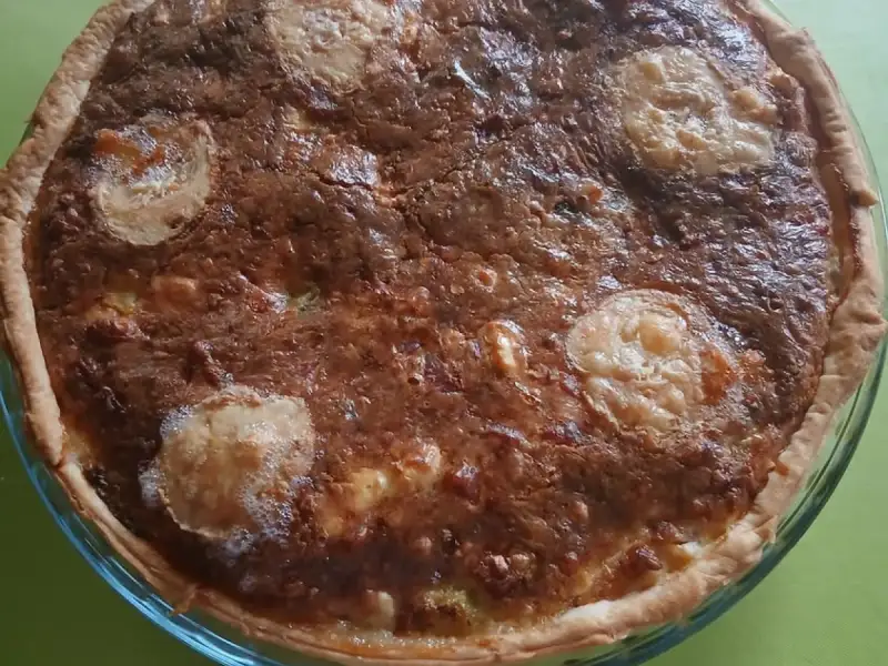 Quiche con sobras del refrigerador bien dorada con rodajas de queso de cabra, en un molde de vidrio