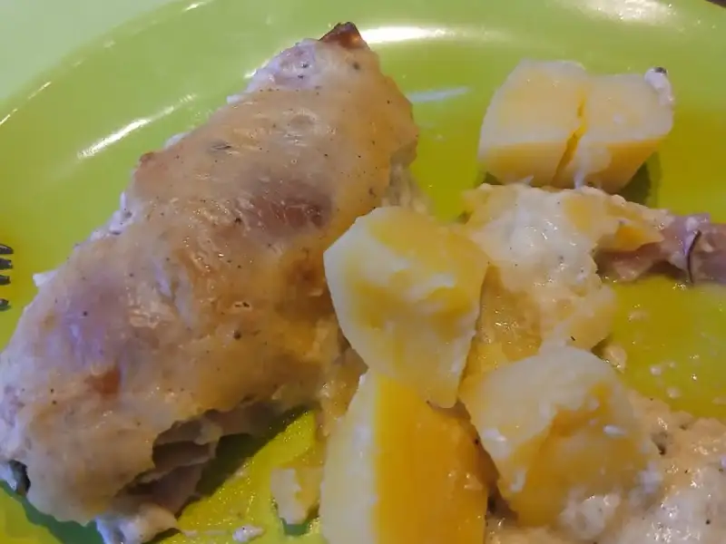 Rollitos de pollo con jamón dorados al horno con papas a la crema en un plato verde